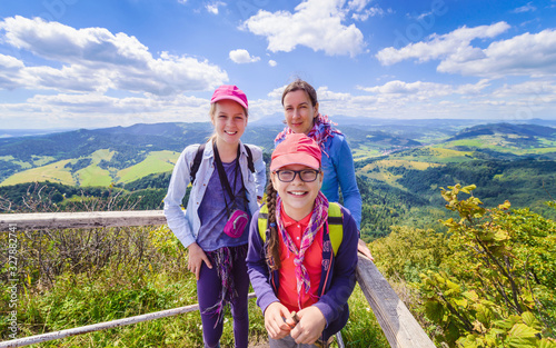 Happy family - mother and two daughters - on a hiking trip to the mountains - on top of a mountain with blue sky and clouds in the background
