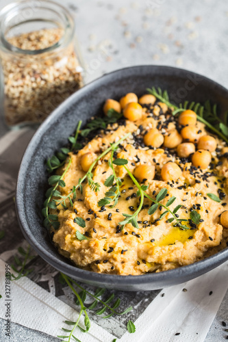 Chickpeas hummus in the black bowl decorated with sesame seeds and chickpeas greens. Vegan recipes, plant-based dishes. Green living concept. Organic food. Vegetarian