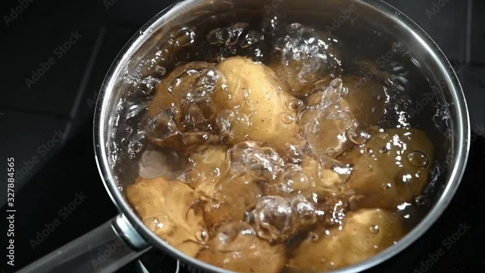Fresh baby potatoes in their skins cooking in a pot of boiling water being lifted out with a metal draining ladle and then replaced Fresh baby potatoes in their skins cooking in a pot of boiling water being lifted out with a metal draining ladle and then replaced