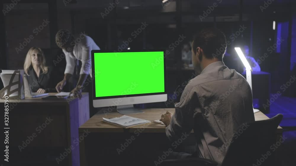 Young employee working on computer with green screen empty monitor.