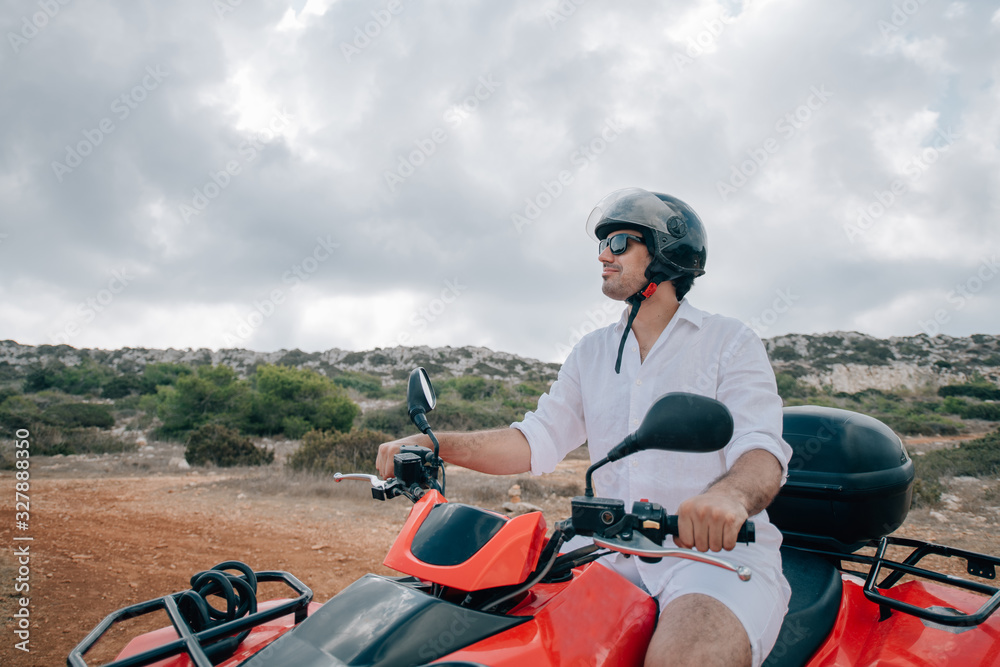 Naklejka premium A man sits on a quad in a helmet and glasses in the mountains