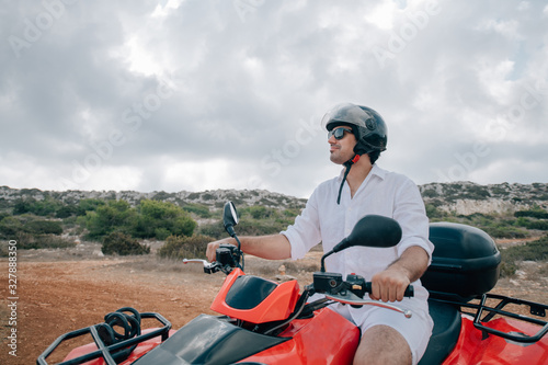 A man sits on a quad in a helmet and glasses in the mountains