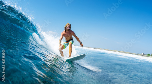 Young man surfs ocean wave in Maldives