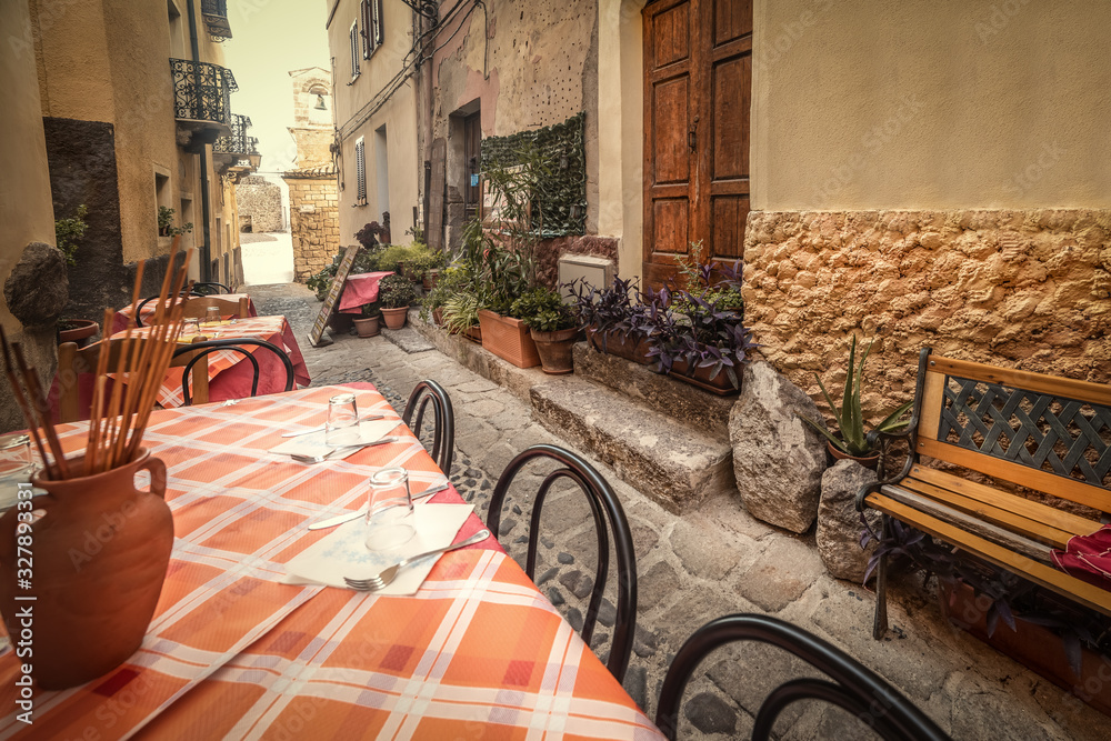 Naklejka premium Tables and chairs in a narrow alley in old town Castelsardo