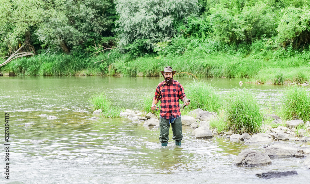 Fisher masculine hobby. Fish on hook. Brutal man wear rubber boots stand in river water. Satisfied fisher. Fishing requires you to be mindful and fully present in moment. Fisher fishing equipment Fisher masculine hobby. Fish on hook. Brutal man wear rubber boots stand in river water. Satisfied fisher. Fishing requires you to be mindful and fully present in moment. Fisher fishing equipment