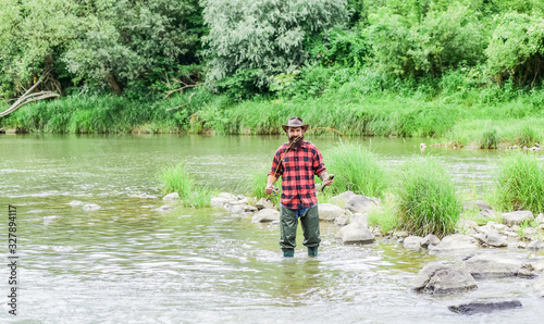 Fisher masculine hobby. Fish on hook. Brutal man wear rubber boots stand in river water. Satisfied fisher. Fishing requires you to be mindful and fully present in moment. Fisher fishing equipment