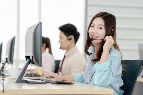 Beautiful business people in headsets are using computers and smiling while working in office.