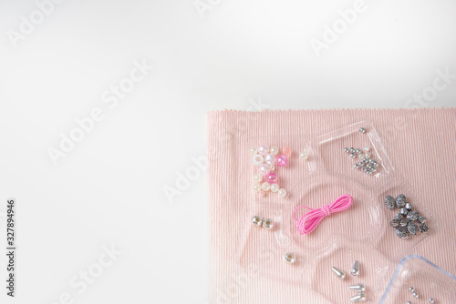 background of pink fabric with accessories for weaving with beads with a container for beads