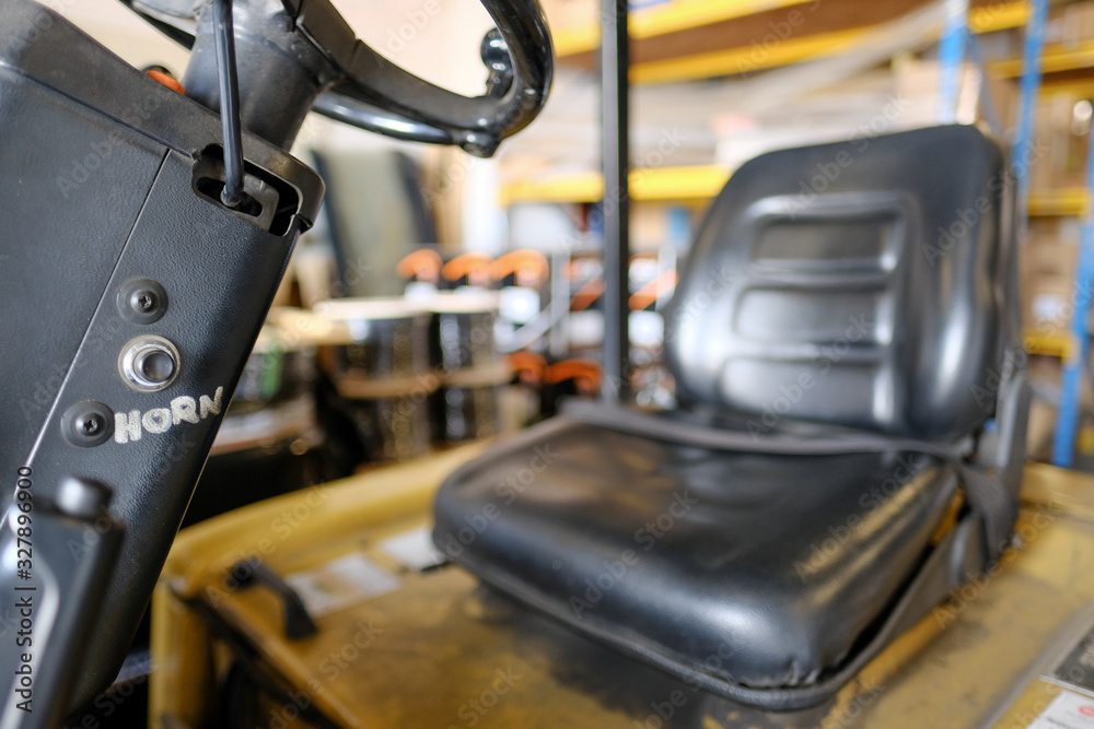 Shallow focus of a hand-written horn sign seen on the steering column of a forklift. The out of focus single seat is also seen, located in the warehouse bay.