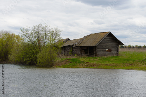 Old abandoned wooden house by the pond on a cloudy spring day © alexnikit