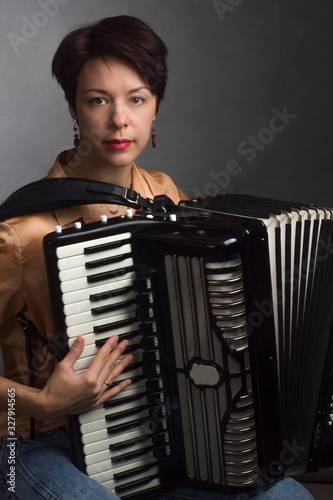A brunette in a gold shirt, with short haircut, on a light gray background of the Studio. With accordion musician