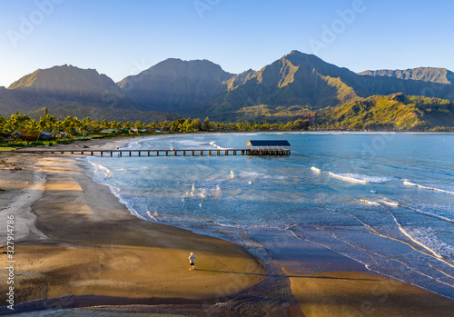 Aerial image at sunrise off the coast over Hanalei Bay and pier on Hawaiian island of Kauai with a man standing alone on the beach photo