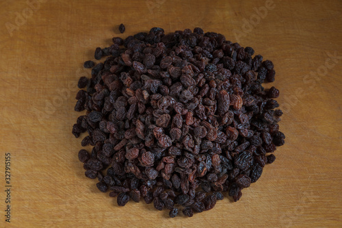 Large raisins are piled in the middle of a light wooden table.