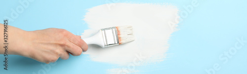 Female hand holding brush on blue background with white paint strokes