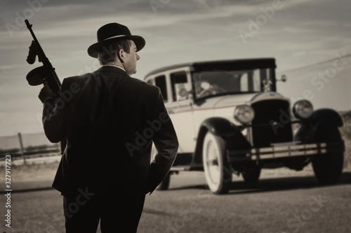 Gangster standing on a road, with a vintage car in the background photo