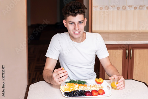 A teenage boy eating fruit at home and drinking orange juice, even though the guy is not a vegetarian but still loves to eat fruit