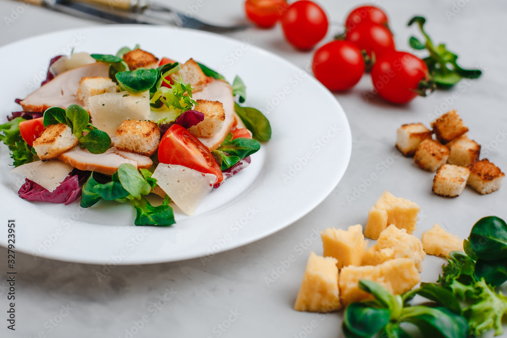 Fresh Caesar salad with delicious chicken breast, spinach, cabbage, arugula, Parmesan and cherry tomatoes on a light background. Caesar sauce, lemon, broken cheese. The concept of healthy and dietary Fresh Caesar salad with delicious chicken breast, spinach, cabbage, arugula, Parmesan and cherry tomatoes on a light background. Caesar sauce, lemon, broken cheese. The concept of healthy and dietary