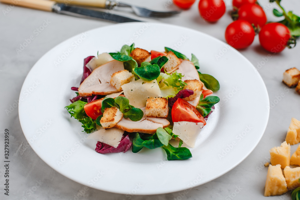 Fresh Caesar salad with delicious chicken breast, spinach, cabbage, arugula, Parmesan and cherry tomatoes on a light background. Caesar sauce, lemon, broken cheese. The concept of healthy and dietary Fresh Caesar salad with delicious chicken breast, spinach, cabbage, arugula, Parmesan and cherry tomatoes on a light background. Caesar sauce, lemon, broken cheese. The concept of healthy and dietary