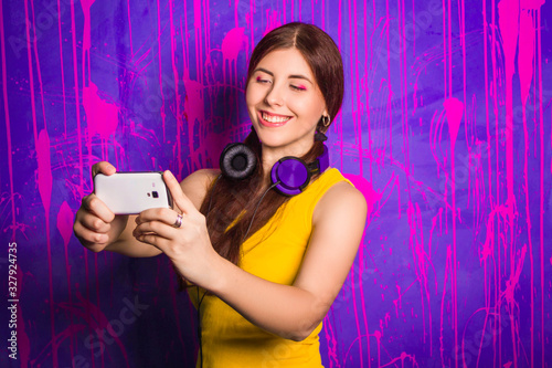 Attractive, beautiful woman with long hair and headphones on her neck, makes selfie while standing on an abstract, purple background.