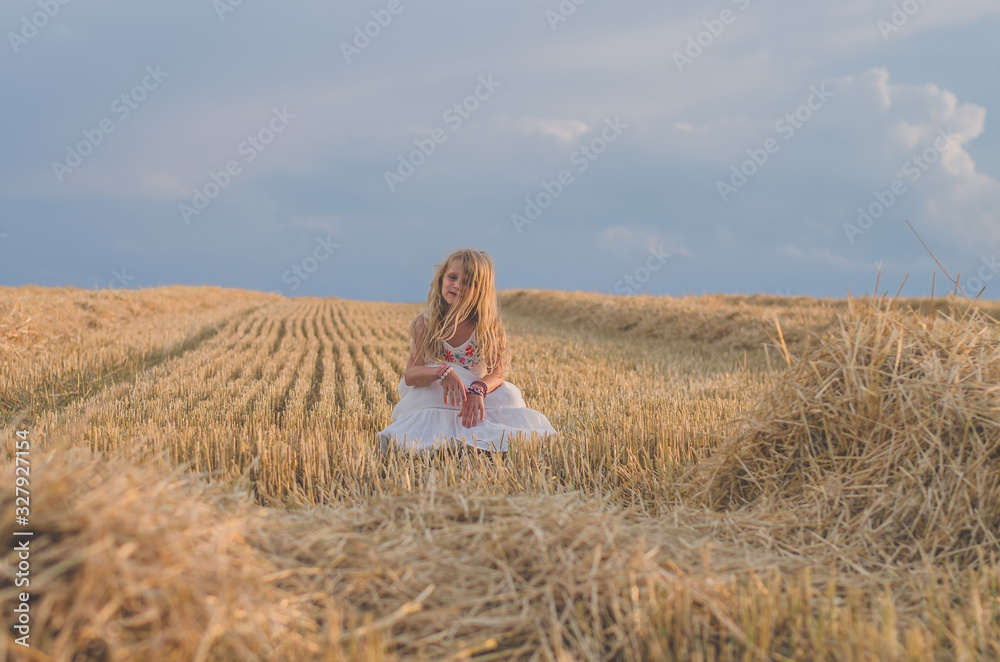 innocent beautiful girl sitting in summer harvester field alone