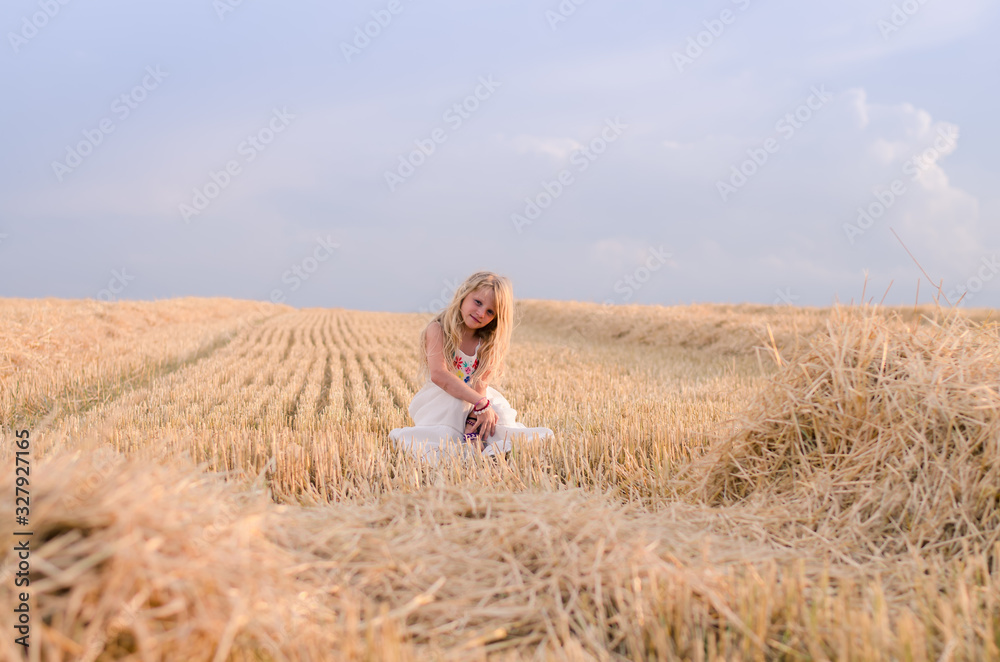 innocent beautiful girl sitting in summer harvester field alone