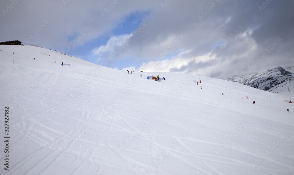 Skiers and snowboarders on trace for ski prepared by snowcat and blue sky with dark clouds