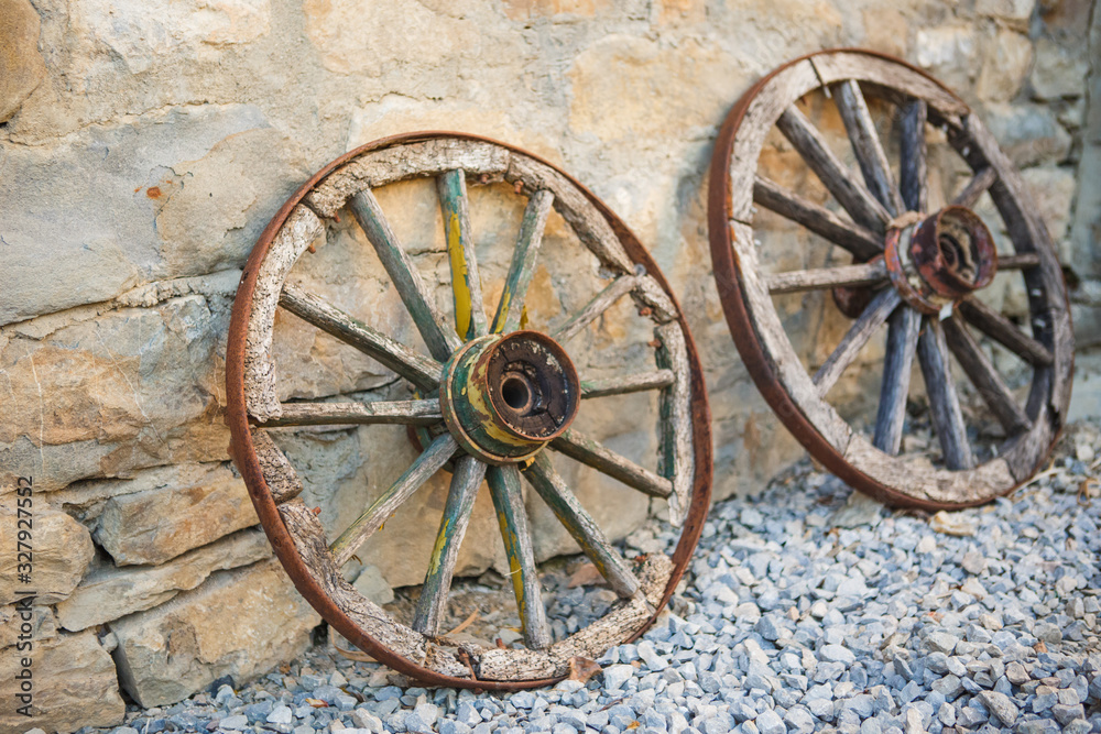 Old wooden cart wheels. Vintage wheels from a horse drawn cart are leaning against a stone wall