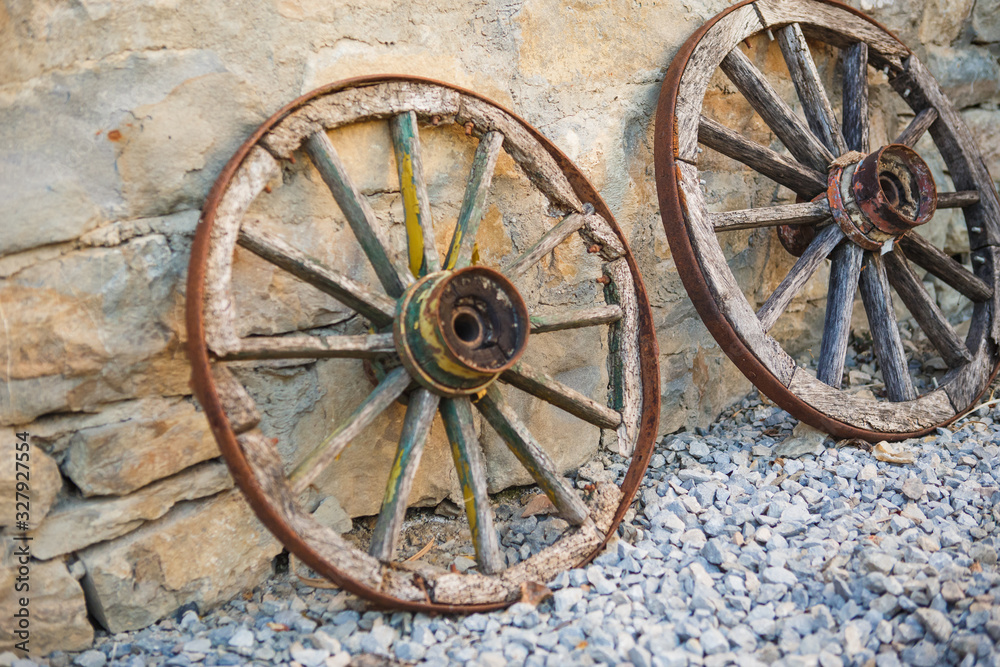 Old wooden cart wheels. Vintage wheels from a horse drawn cart are leaning against a stone wall
