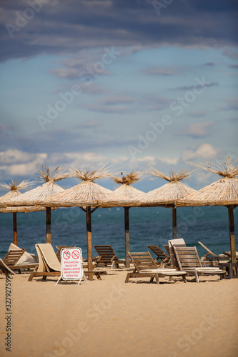 Fototapeta Naklejka Na Ścianę i Meble -  Straw beach umbrellas and wooden sun beds on a sandy beach against the sea. Beach infrastructure in Bulgaria with the inscription: 