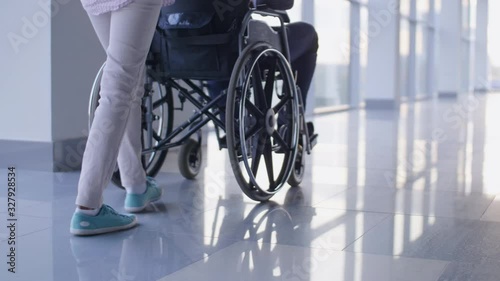 Low-section shotof nurse pushing driving wheelchair with handicapped patient through the corridor with mirror floor
