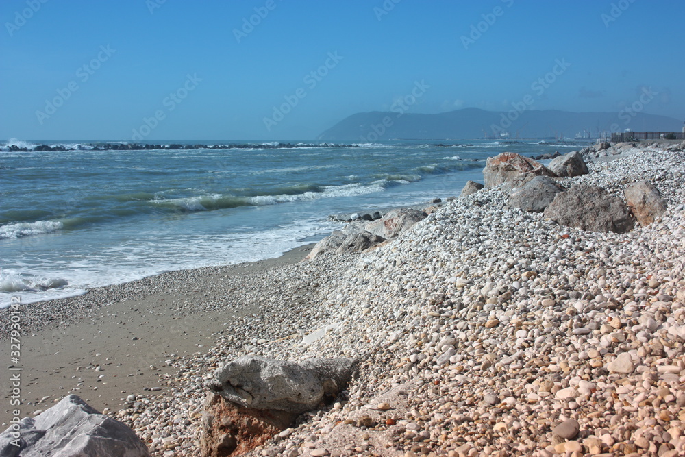 sea ​​with sandy beach and rocks with a view of the fiat tower in massa carrara in tuscany in front of the don gnocchi hospital