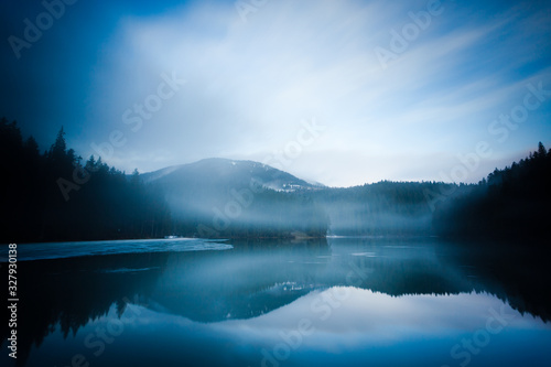 Mountain lake surrounded by forest covered in fog