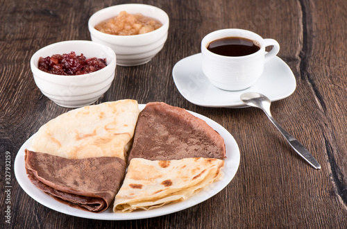 Pancakes on a white plate, apple jam of different varieties and coffee over a wooden background.