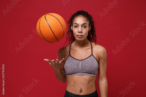 Young african american sports fitness basketball player woman in sportswear working out isolated on red wall background studio portrait. Sport exercises healthy lifestyle concept. Throwing up ball.