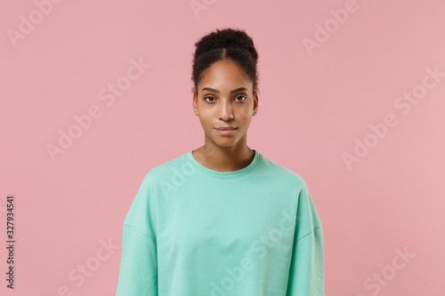 Beautiful young african american woman girl in green sweatshirt posing isolated on pastel pink background studio portrait. People sincere emotion lifestyle concept. Mock up copy space. Looking camera.