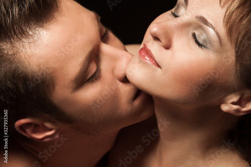 Close up of beautiful sexy couple embracing and enjoying each other closeness. Handsome gentleman hugging girl from behind and pressing nose and lips to lady cheek. Concept of love and passion.