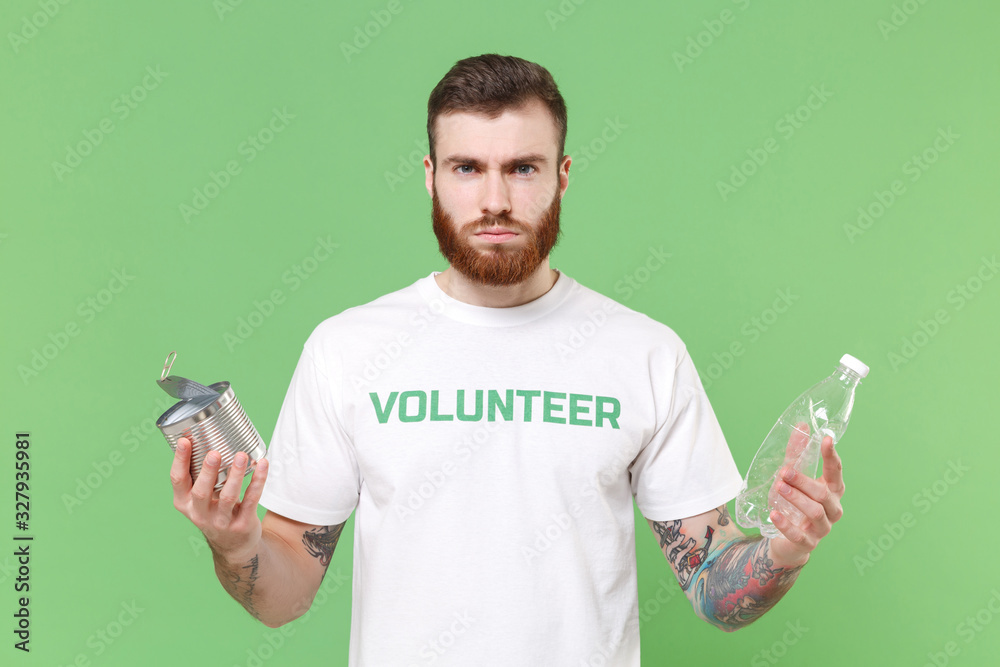 Displeased young bearded man in white volunteer t-shirt isolated on pastel green background. Voluntary free work assistance help charity grace teamwork concept. Hold trash empty plastic bottle tincan. Displeased young bearded man in white volunteer t-shirt isolated on pastel green background. Voluntary free work assistance help charity grace teamwork concept. Hold trash empty plastic bottle tincan.