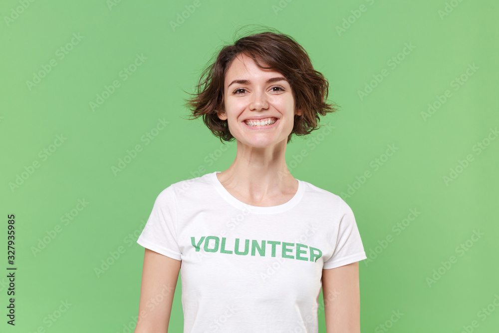 Smiling young brunette woman in white volunteer t-shirt isolated on pastel green wall background studio portrait. Voluntary free work assistance help charity grace teamwork concept. Looking camera. Smiling young brunette woman in white volunteer t-shirt isolated on pastel green wall background studio portrait. Voluntary free work assistance help charity grace teamwork concept. Looking camera.