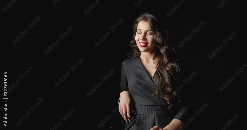Elegant young woman with romantic makeup in black dress posing to camera on black background Elegant young woman with romantic makeup in black dress posing to camera on black background