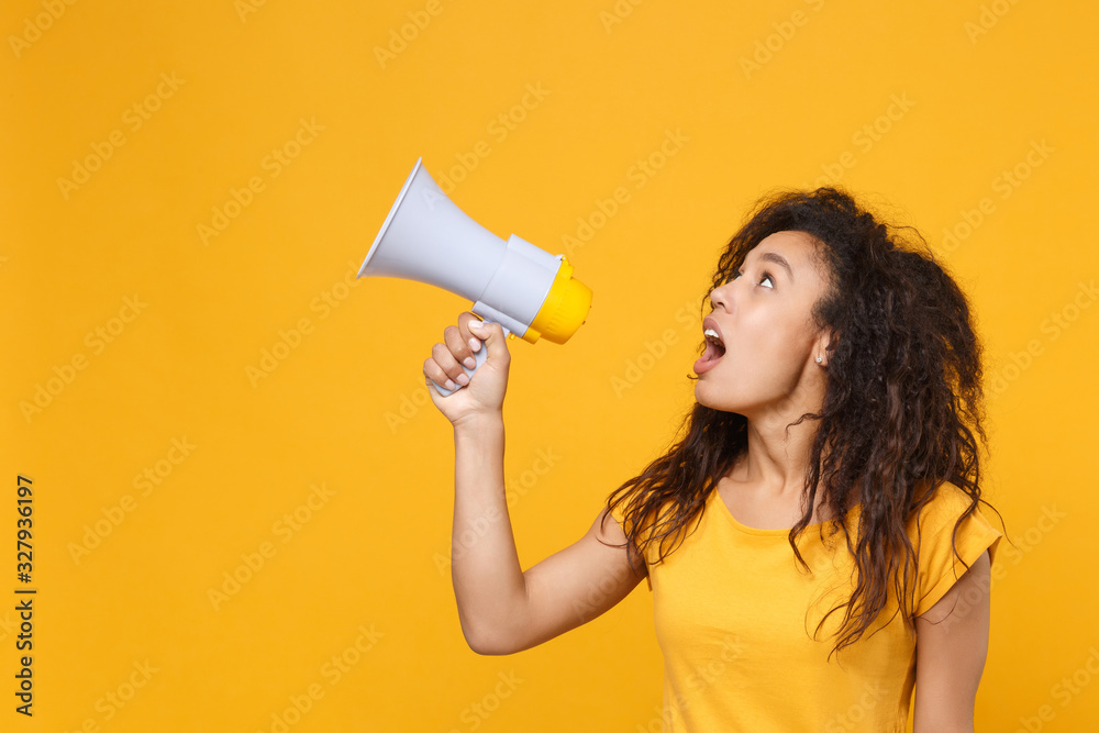 Amazed young african american woman girl in casual t-shirt posing isolated on yellow orange background studio portrait. People lifestyle concept. Mock up copy space. Scream in megaphone, looking up. Amazed young african american woman girl in casual t-shirt posing isolated on yellow orange background studio portrait. People lifestyle concept. Mock up copy space. Scream in megaphone, looking up.