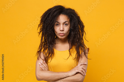 Dissatisfied young african american woman girl in casual t-shirt posing isolated on yellow orange wall background studio portrait. People lifestyle concept. Mock up copy space. Holding hands crossed.