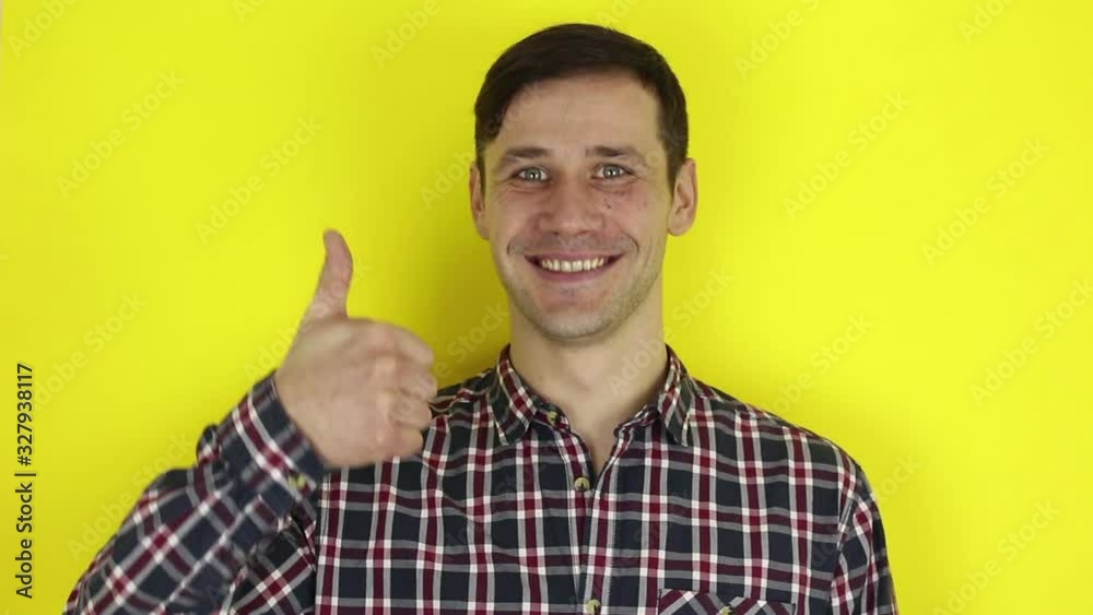 Funny handsome guy smiles and shows thumb up. Portrait of a young guy, he smiles and shows thumb up. Portrait on yellow background. Funny handsome guy smiles and shows thumb up. Portrait of a young guy, he smiles and shows thumb up. Portrait on yellow background.