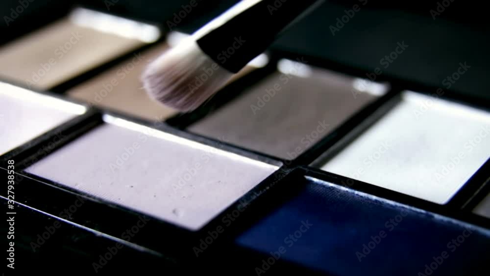 Footage of colorful palette with paints and shadows for makeup. Professional makeup artist or visagiste holding palette and picking right color with brush. Beauty, makeup and fashion concept