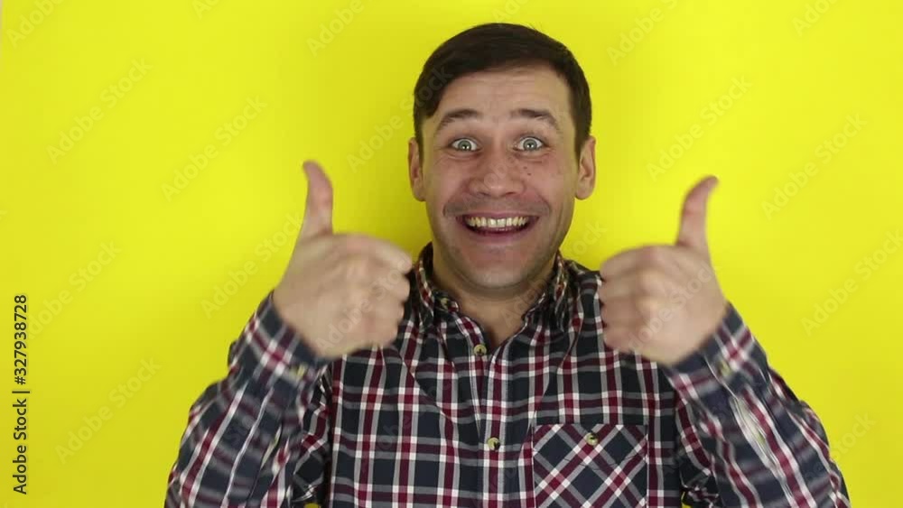Funny handsome guy smiles and shows thumb up with both hands. Portrait of a young guy, he smiles and shows thumb up with both hands. Portrait on yellow background. Funny handsome guy smiles and shows thumb up with both hands. Portrait of a young guy, he smiles and shows thumb up with both hands. Portrait on yellow background.