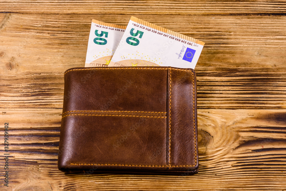 Brown leather wallet with fifty euro banknotes on the wooden background. Top view Brown leather wallet with fifty euro banknotes on the wooden background. Top view