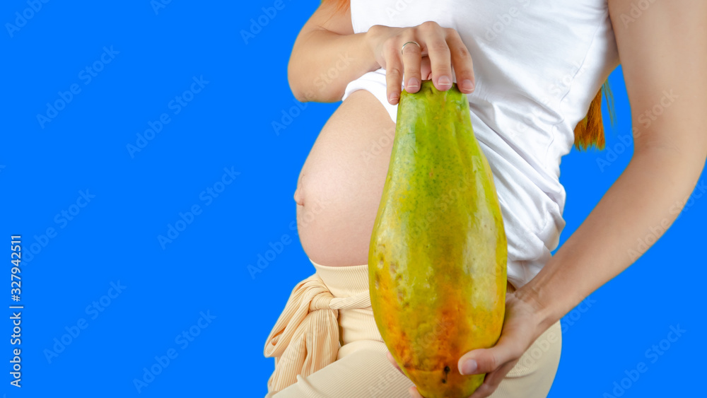 A happy pregnant young woman holding a papaya next to her belly showing