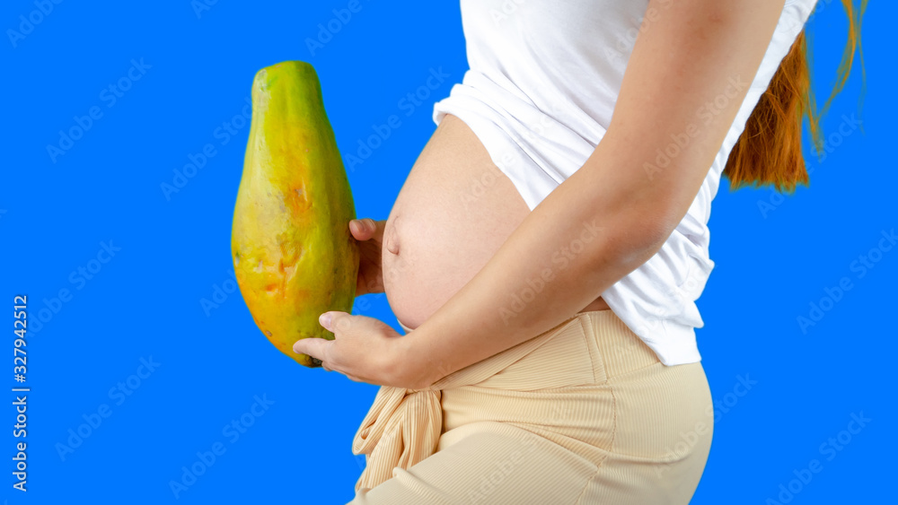 A happy pregnant young woman holding a papaya next to her belly showing the size of the baby
