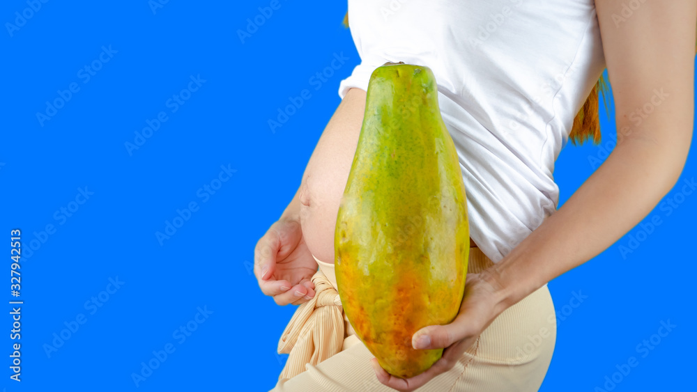 A happy pregnant young woman holding a papaya next to her belly showing