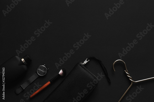 Accessories for women's beauty. Make up brush, watch, nail polish and hair straightener, all on a black background with top view and copy space. Minimalist black trend 2020 and cosmetics background.