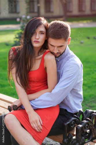 Beautiful couple of man and woman sitting on a bench in a park. Romantic theme with a girl and a guy. Spring Summer theme relationship, love, Valentine's day